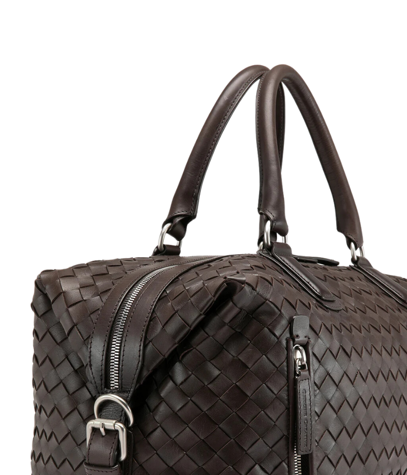 Handwoven brown leather Armor 019 Travel Bag with durable handles, an adjustable shoulder strap, side buckles, and a spacious interior with a side zipper pocket. Made in Italy.