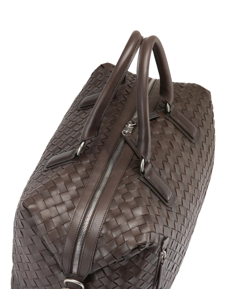 Handwoven brown leather Armor 019 Travel Bag with durable handles, an adjustable shoulder strap, side buckles, and a spacious interior with a side zipper pocket. Made in Italy.