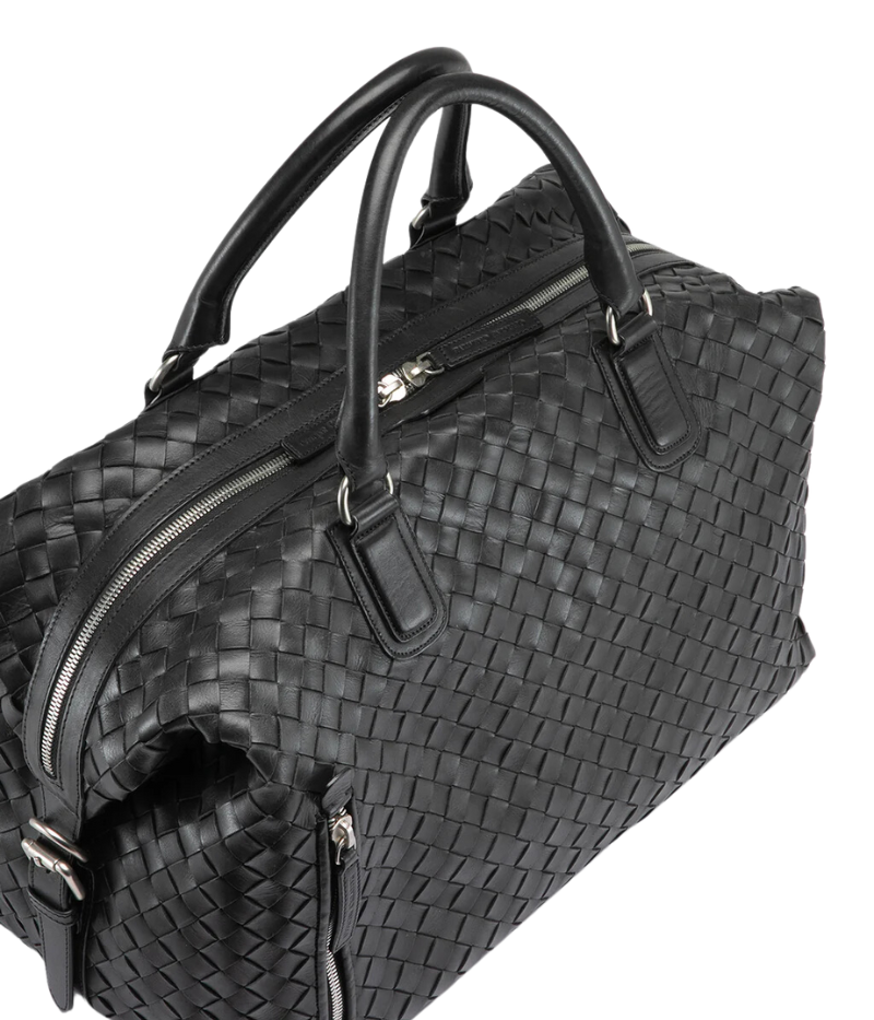 Handwoven black leather Armor 019 Travel Bag with durable handles, an adjustable shoulder strap, side buckles, and a spacious interior with a side zipper pocket. Made in Italy.