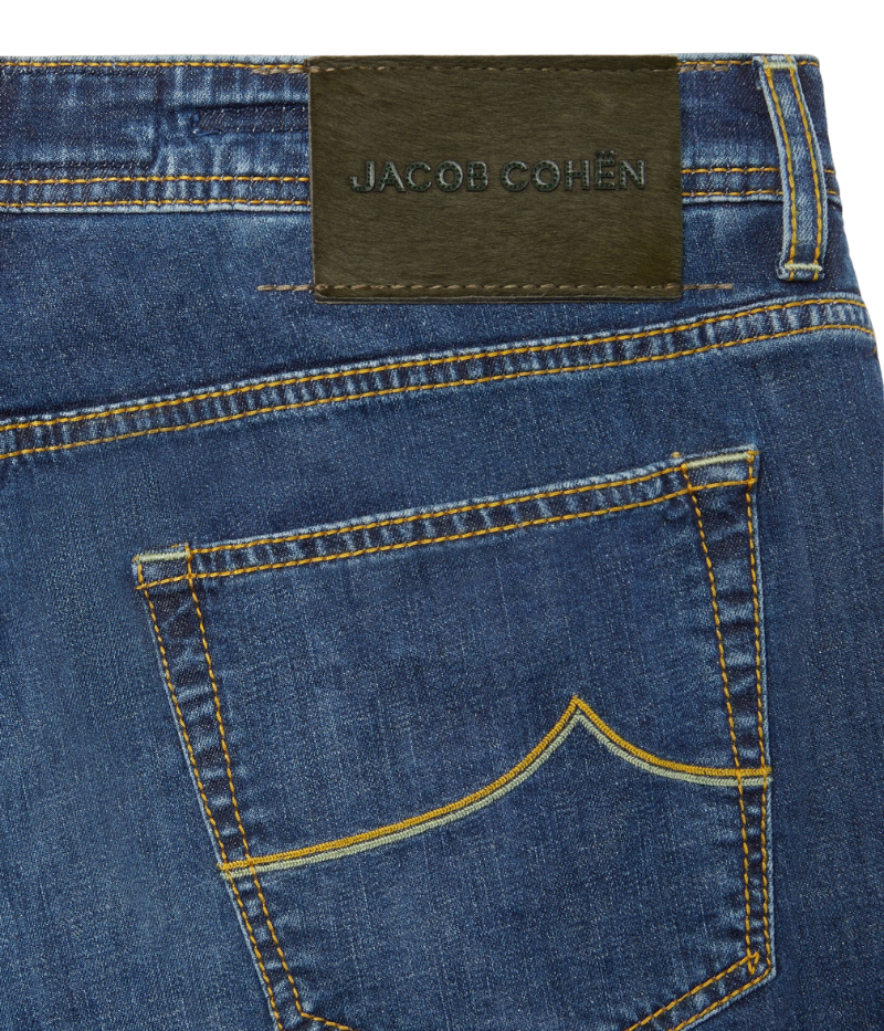 Close-up of the Bard 5-Pocket Jeans in dark blue stonewashed stretch denim, featuring a regular-slim fit. Crafted from a cotton-linen blend for comfort and durability, these jeans include an embroidered logo on the fifth pocket, a World print bandana, and a spool of thread. Finished with Jacob Cohën’s signature fragrance. Made in Italy.