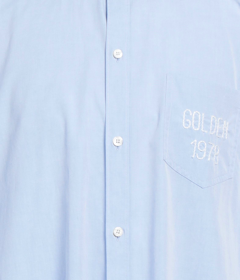 Close-up of the Golden Goose Journey Shirt, showcasing the embroidered chest pocket detail on soft blue cotton fabric. The subtle stitching adds a unique touch to this classic button-up shirt, elevating it with understated charm.